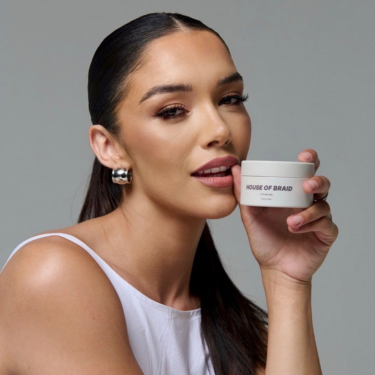 Woman holding a jar of 'House of Braids' product against a gray background